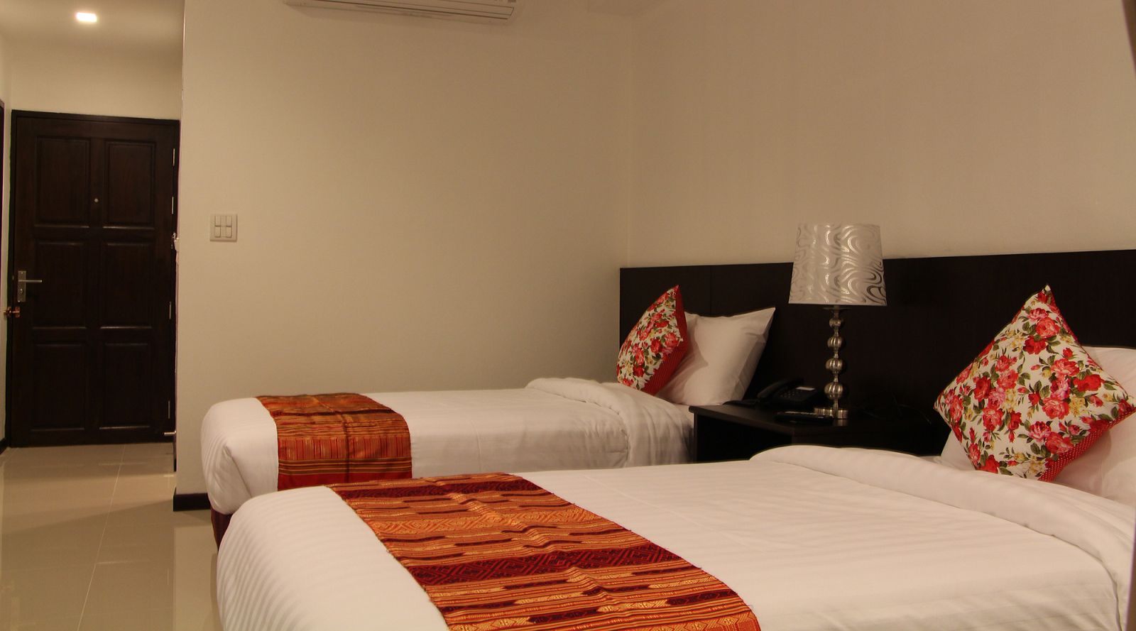 Quarto de hotel com duas camas, cada uma com colcha estampada, mesa de cabeceira com abajur e almofadas florais.