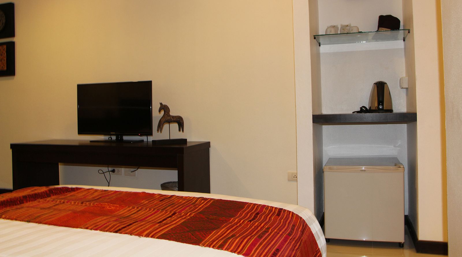 A hotel room with a bed, a television on a desk, a small refrigerator, and a shelf with toiletries.