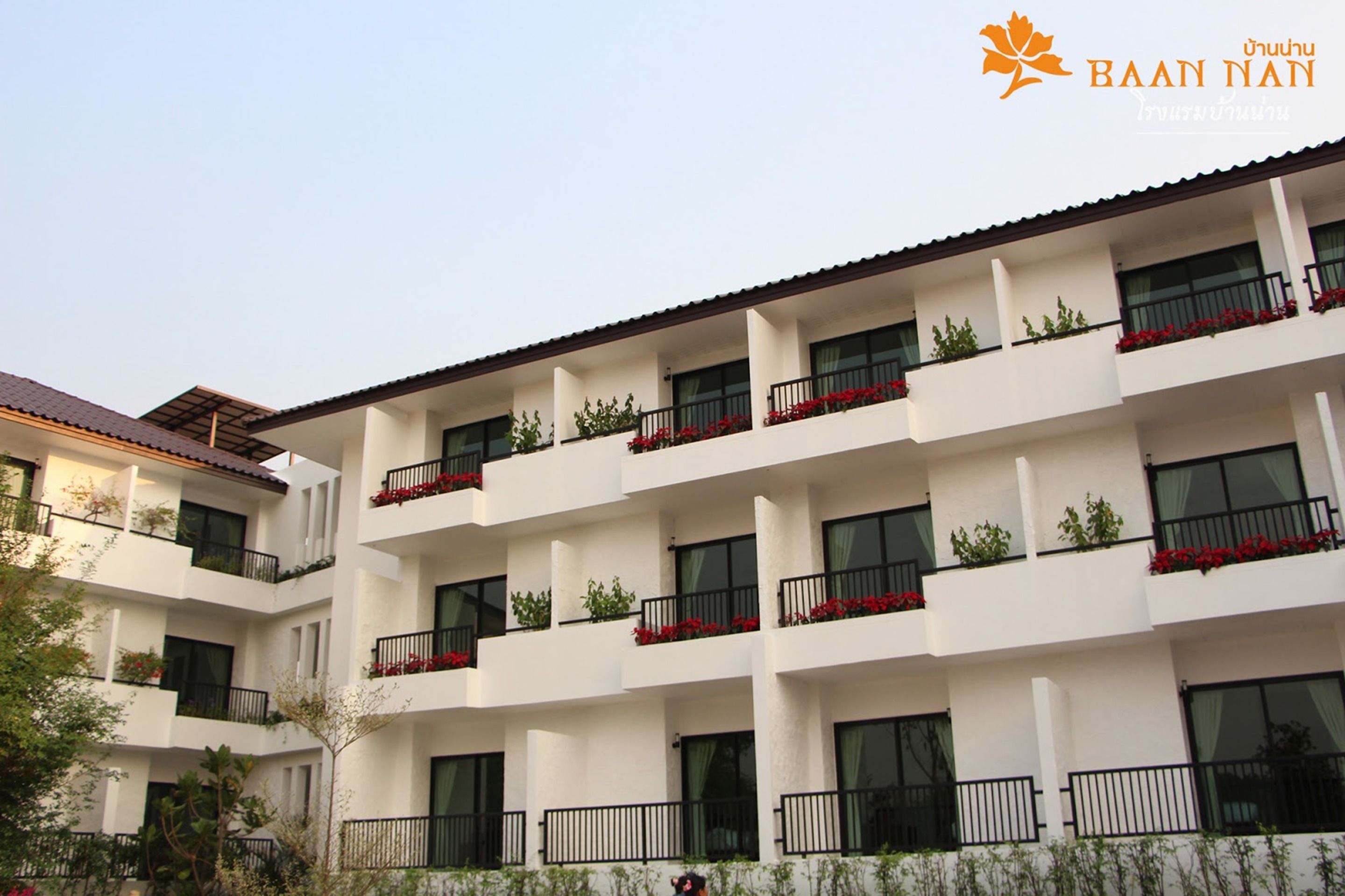 A multi-story hotel with balconies, each with red flowers.