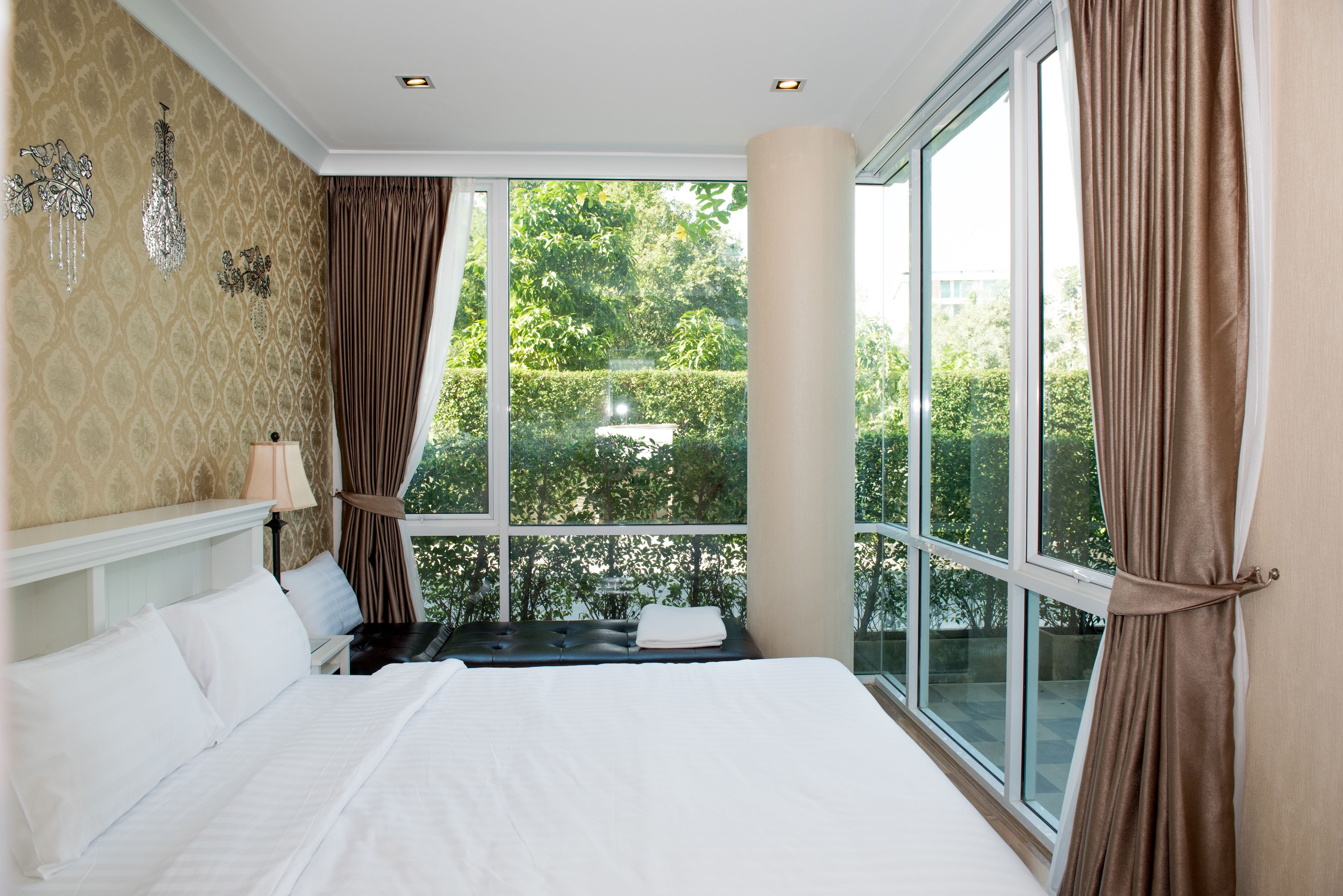 A bedroom with a large window, a bed, and a nightstand.