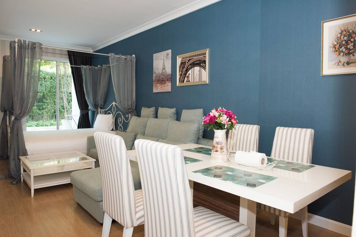 Une pièce avec une table à manger blanche, des chaises à rayures, un canapé et une fenêtre avec des rideaux.