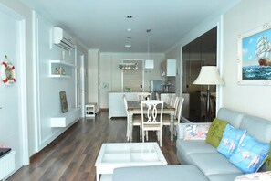 Uma sala de estar moderna com área de jantar, cozinha e vista para o mar por uma grande janela.