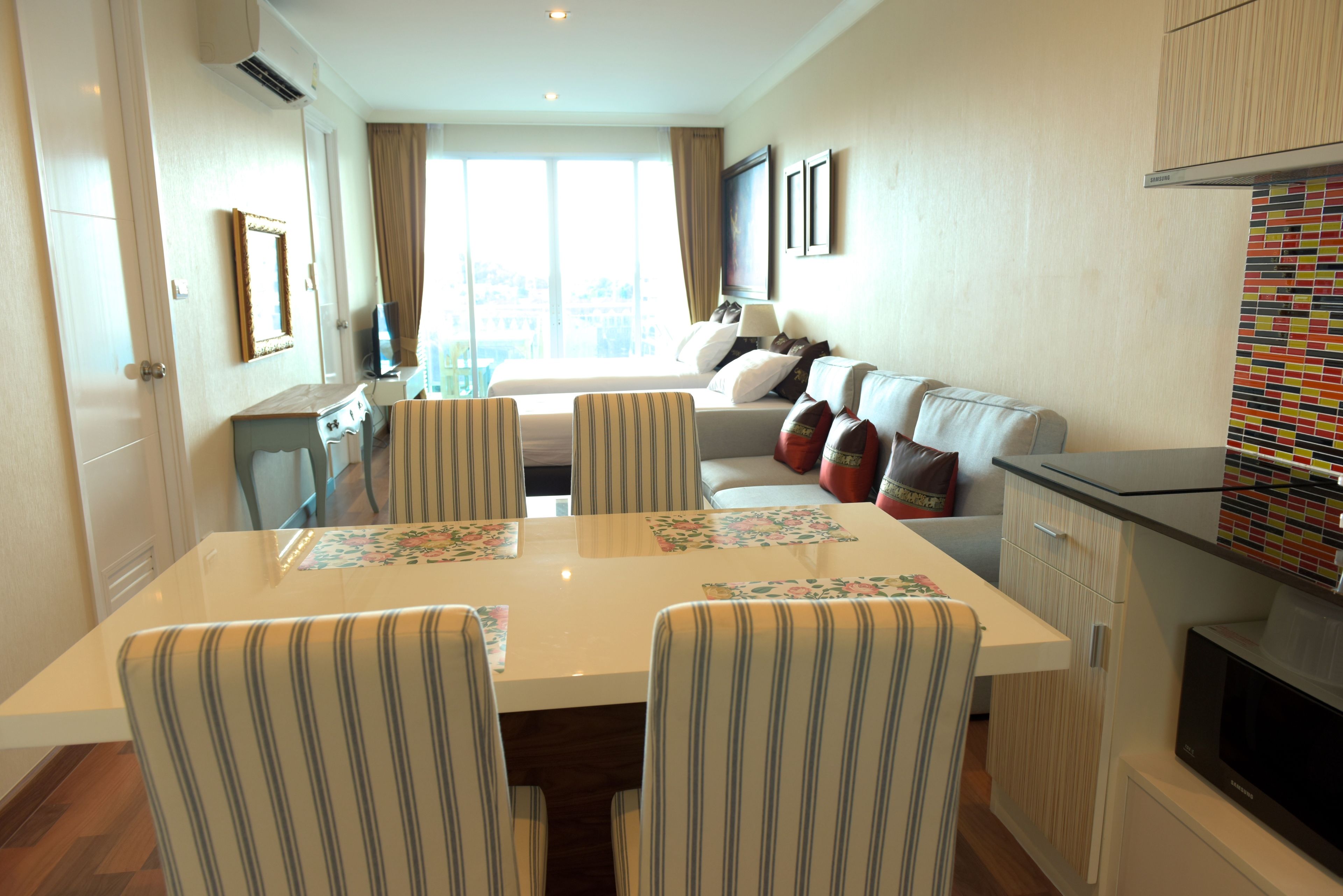 A hotel room with a dining area, a sofa with cushions, a television, and a kitchen area.