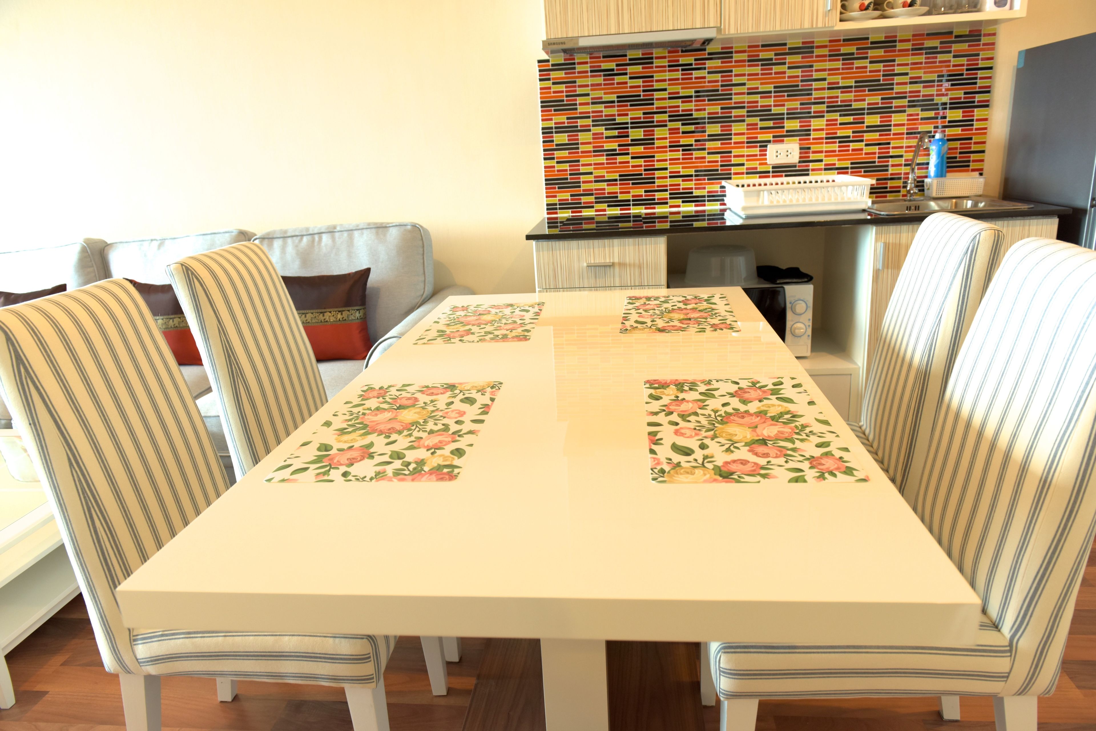 Un comedor con mesa y sillas, una cocina con salpicadero colorido, y un sofá al fondo.