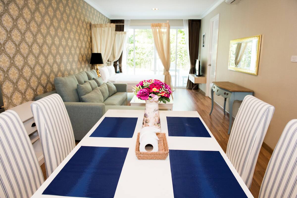 Un salon avec un canapé, une table à manger avec des sets de table bleus, un vase rempli de fleurs et des chaises à rayures.