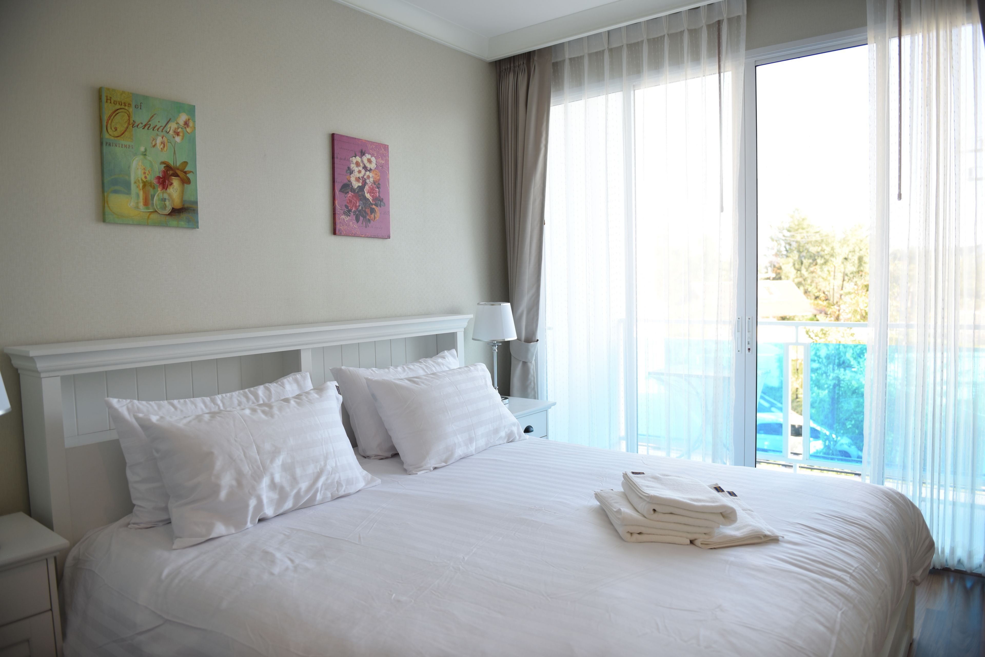 Une chambre d’hôtel avec un grand lit, du linge de lit blanc, une table de chevet avec une lampe et deux œuvres d’art murales.