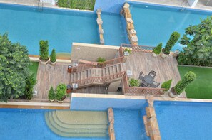 Uma área de piscina no terraço com várias piscinas, um deck de madeira e plantas em vasos.