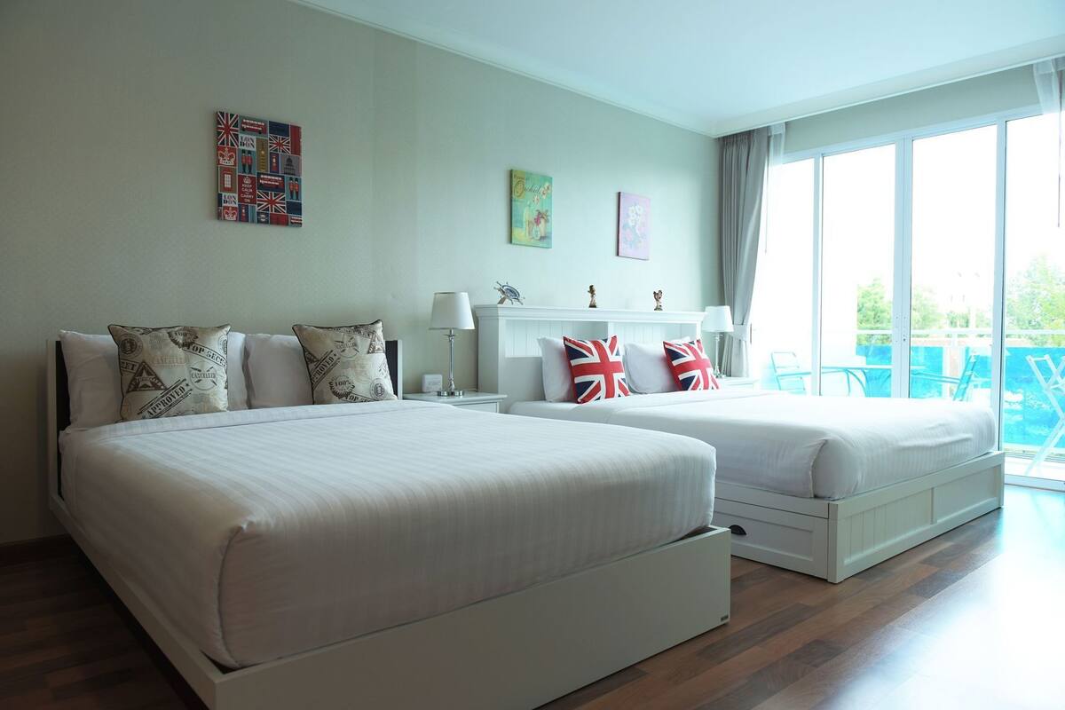 Une chambre d’hôtel avec deux lits, une table de chevet, une lampe, une cheminée et un balcon avec des chaises.