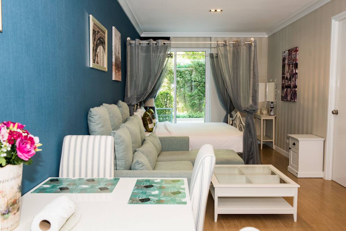 Une chambre à coucher avec un lit, un canapé, une petite table et une fenêtre avec des rideaux.