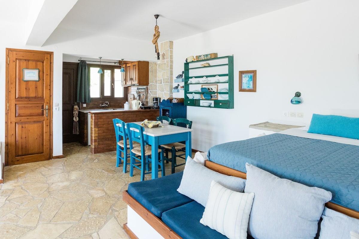 A cozy room with a bed, a dining table with chairs, a kitchen area, and a bathroom.
