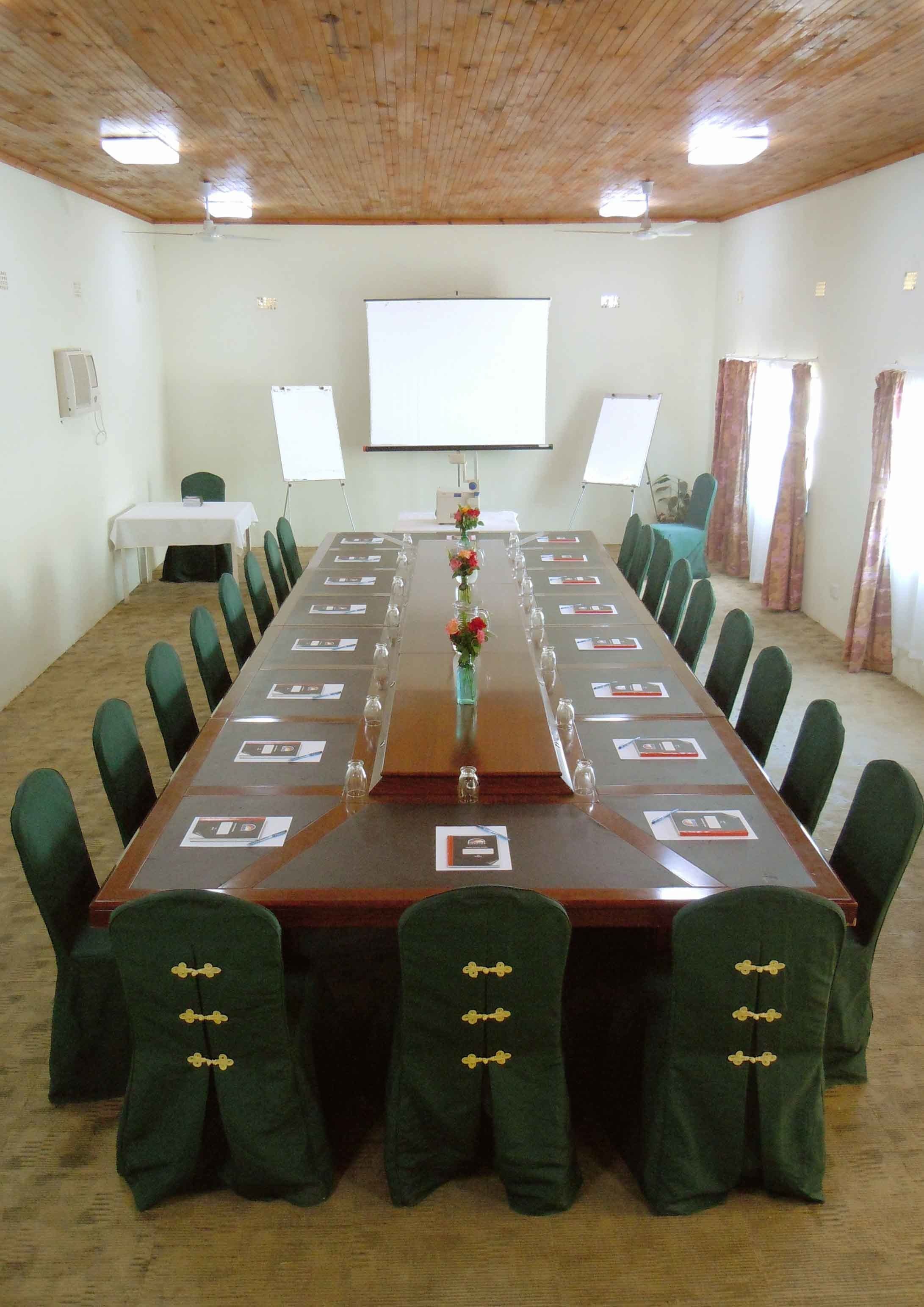 Una sala conferenze con un lungo tavolo, sedie verdi e uno schermo per proiezioni.