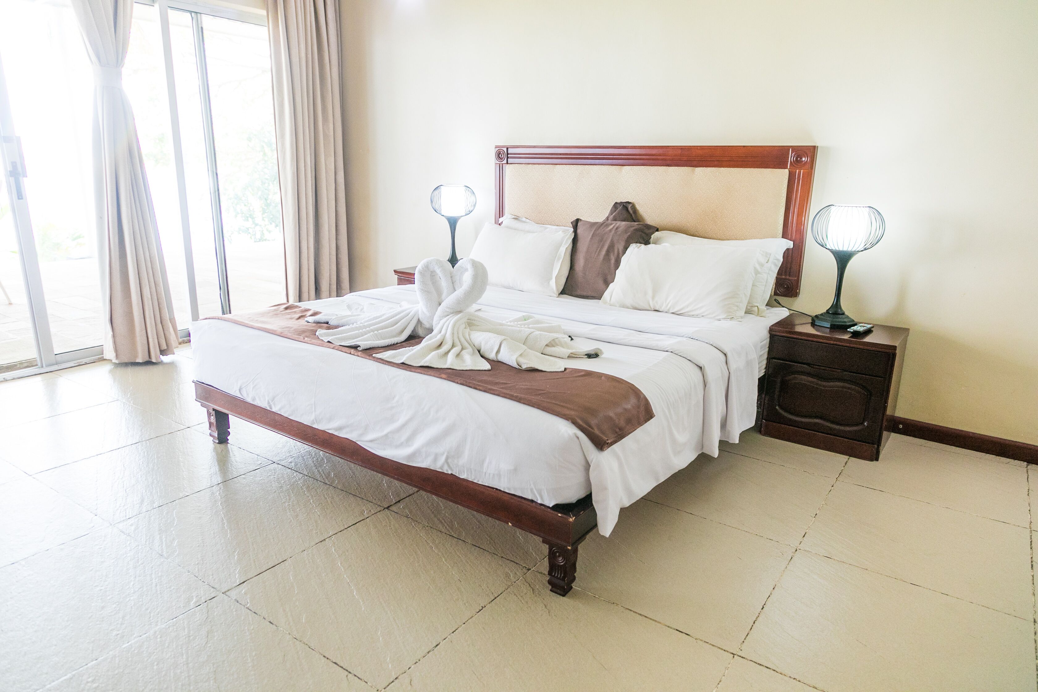 Una cama bien hecha con ropa de cama blanca y marrón, dos lámparas de noche y un cabecero de madera.