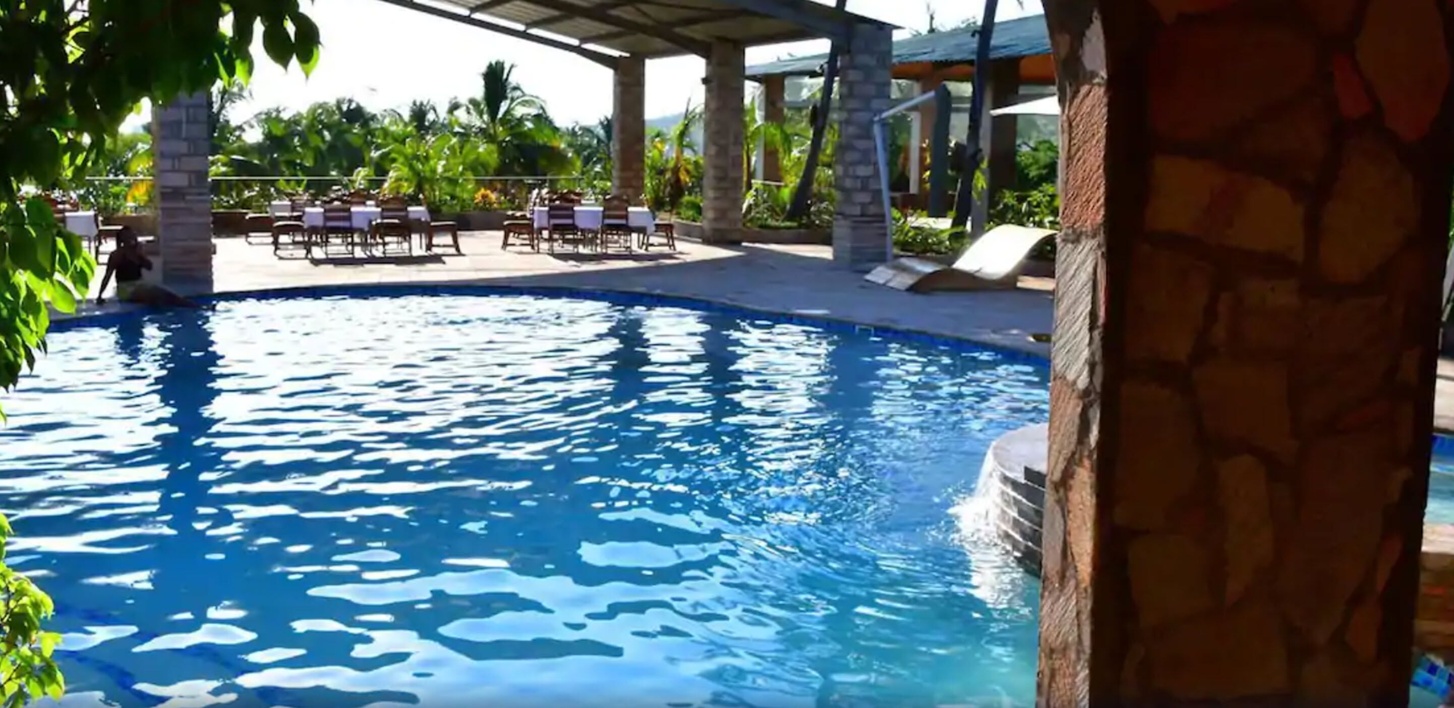 A pool area with lounge chairs and tables, surrounded by greenery.
