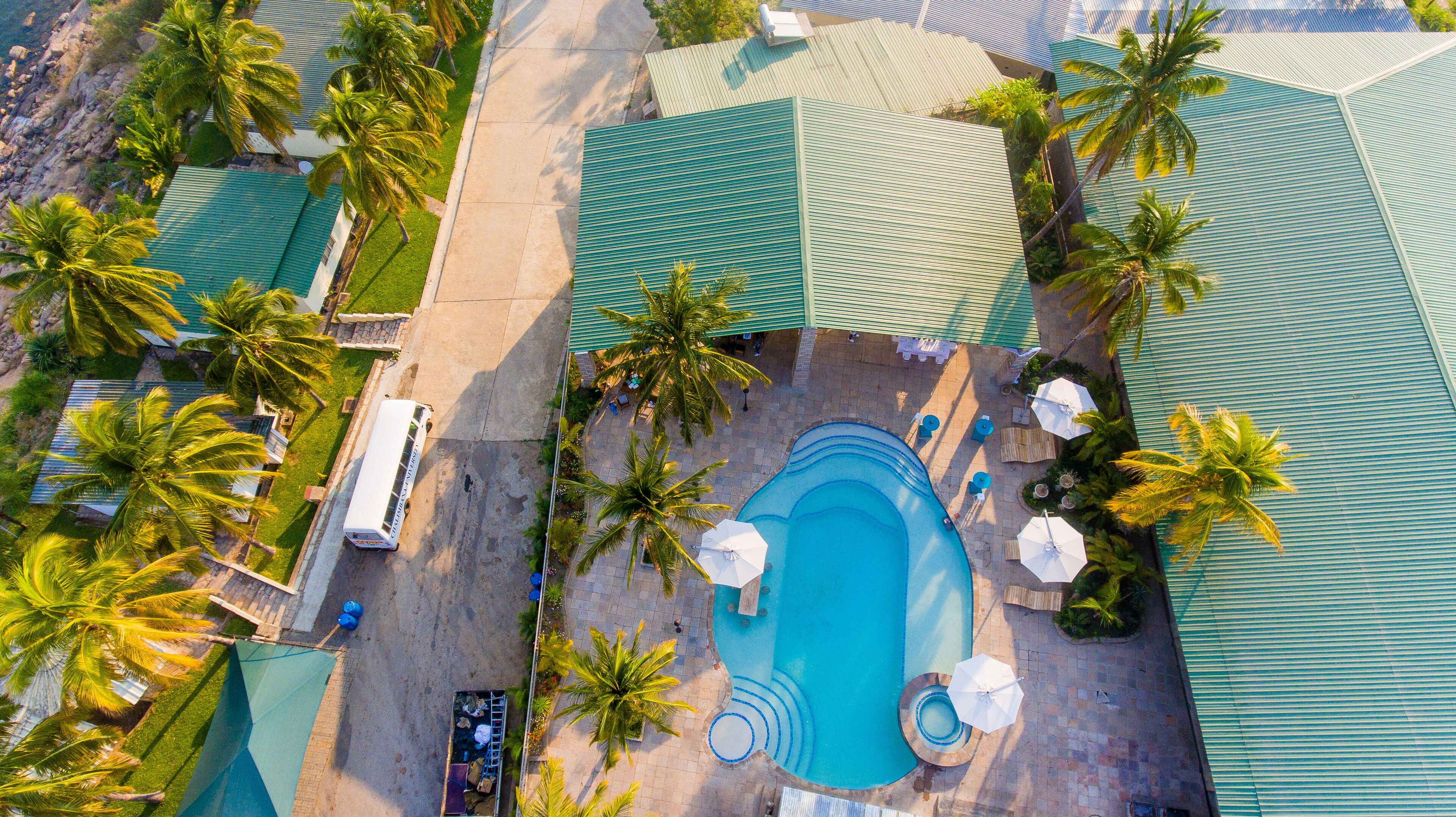 Vista aérea de um resort com piscina, palmeiras e um ônibus.