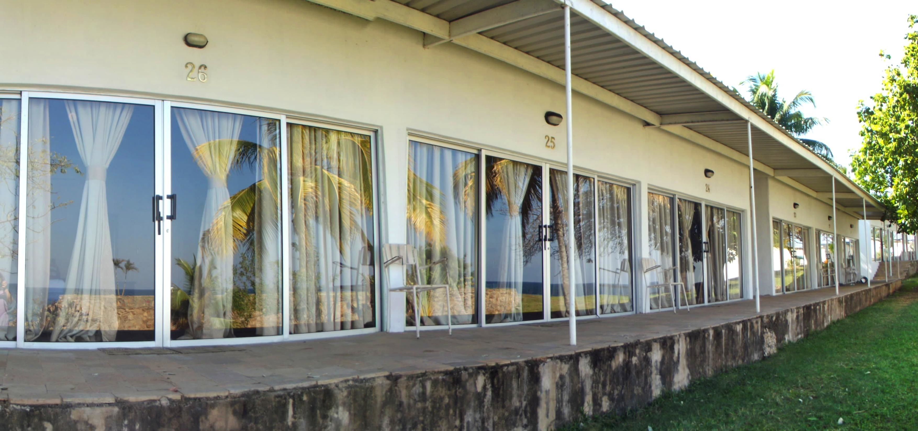 A row of rooms with large windows, numbered 25 and 26, and a covered outdoor area with chairs.