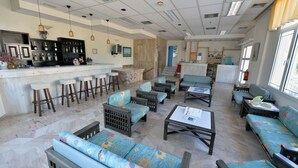 A spacious lounge area with multiple seating options, a bar with stools, and a kitchen area in the background. - Anna Hotel (Hersonissos)