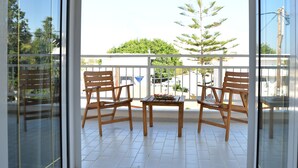 A balcony with wooden chairs and a table, a glass door, and a view of a tree and buildings. - Anna Hotel (Hersonissos)