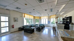 A spacious room with a large window, a fire extinguisher, and a bar area with stools. - Anna Hotel (Hersonissos)