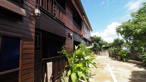 Una casa de madera con balcón, un camino de hormigón y abundante vegetación alrededor.