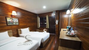 Habitación de hotel con dos camas, paneles de madera, un escritorio pequeño con un cesto de artículos de aseo y un cuadro en la pared.