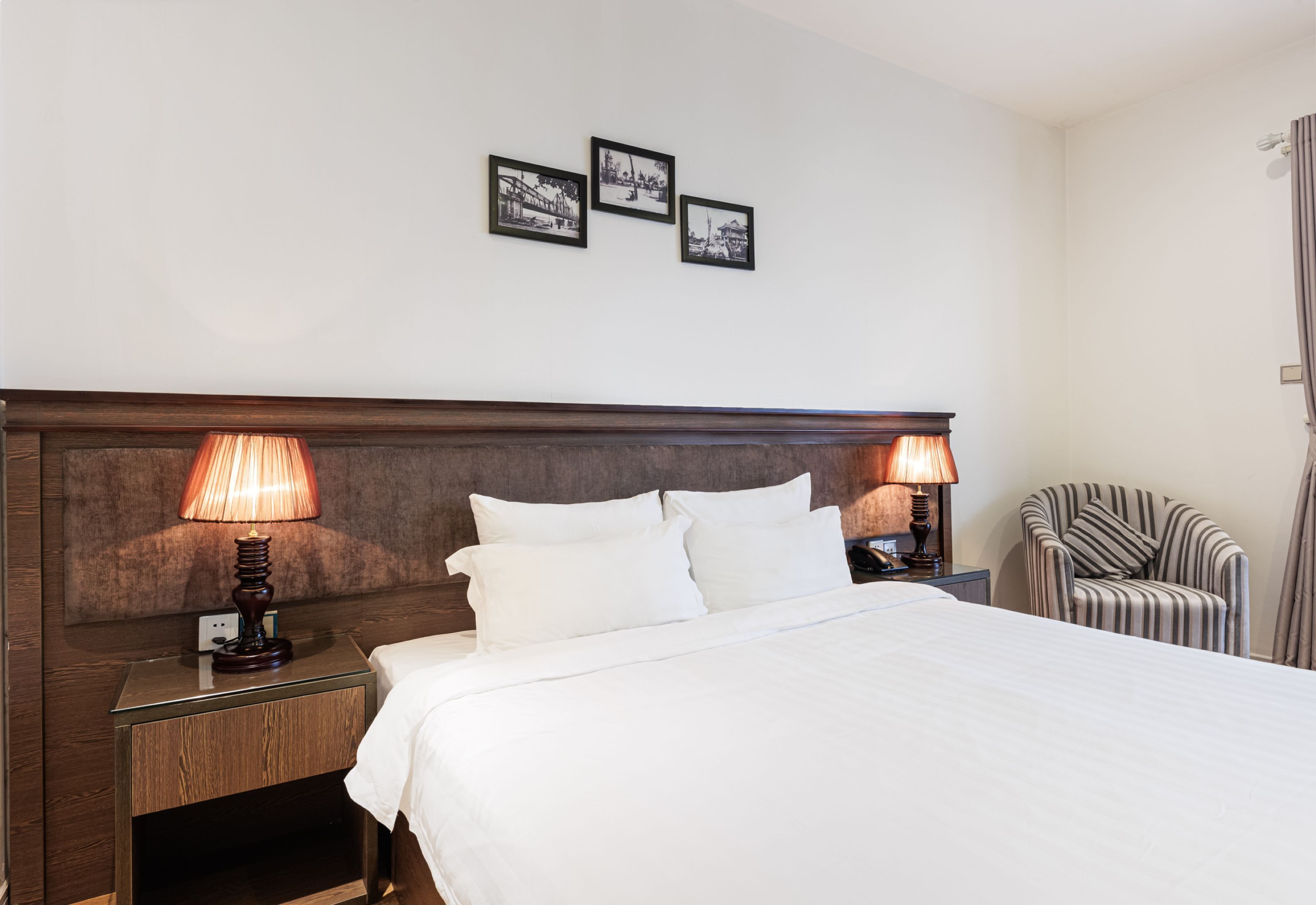 Ein Hotelzimmer mit einem großen Bett, zwei Nachttischlampen, einem Sessel und drei gerahmten Bildern an der Wand.