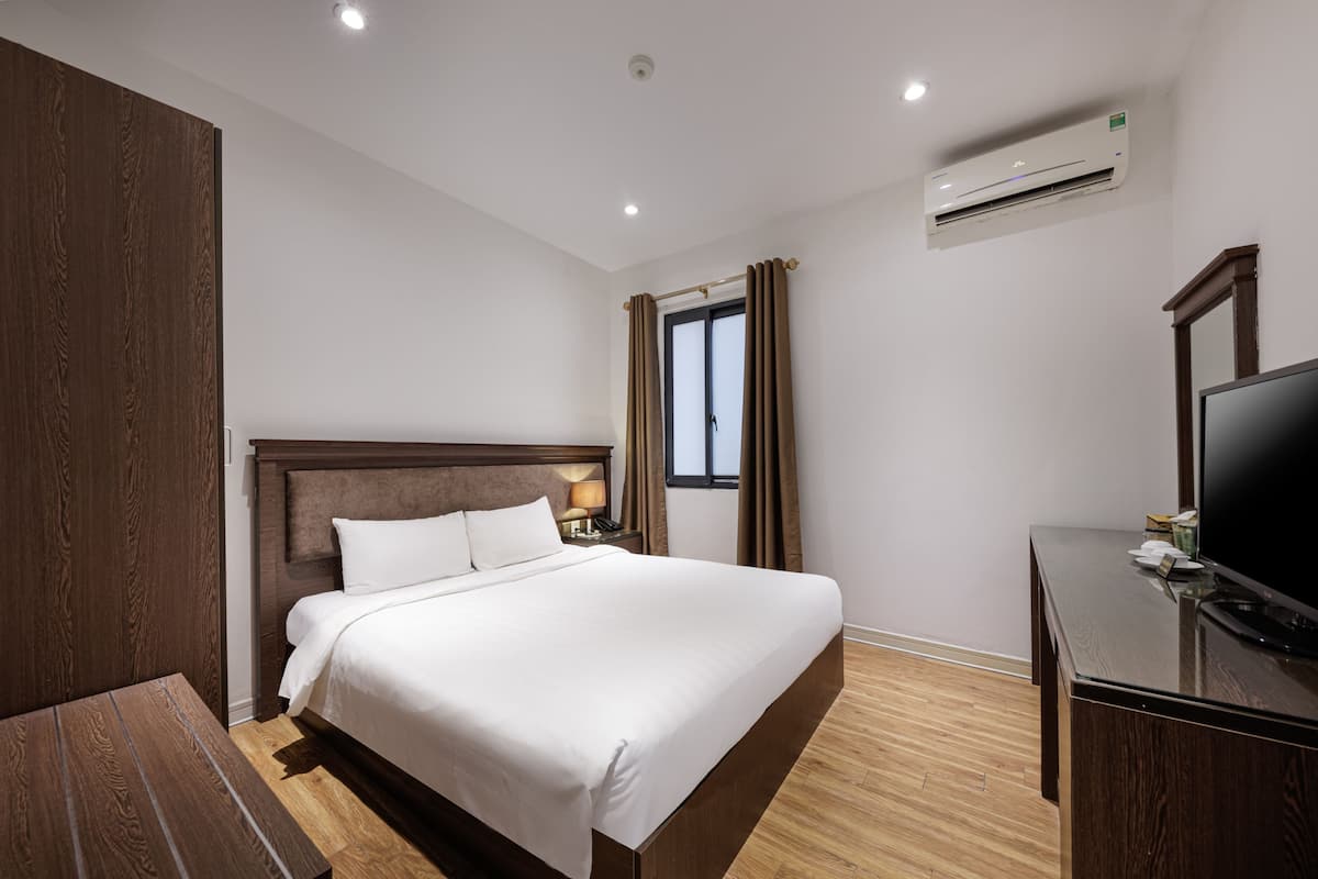 A hotel room with a large bed, a wooden headboard, a flat-screen TV, and an air conditioning unit.