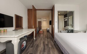 Habitació d'hotel amb un llit, televisió, escriptori, taula de cafè i bany amb un lavabo i mirall.
