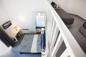 Quarto pequeno com cama, escrivaninha e cadeira.