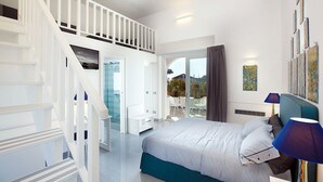 A modern bedroom with a bed, a nightstand, a lamp, and a staircase leading to a balcony. - Casa Colarusso (Massa Lubrense)