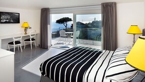 A hotel room with a bed, a desk, two chairs, a balcony with a table and chairs, and a view of the sea. - Casa Colarusso (Massa Lubrense)