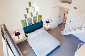 Quarto moderno com cama, abajures, cabeceira azul e arte abstrata na parede.