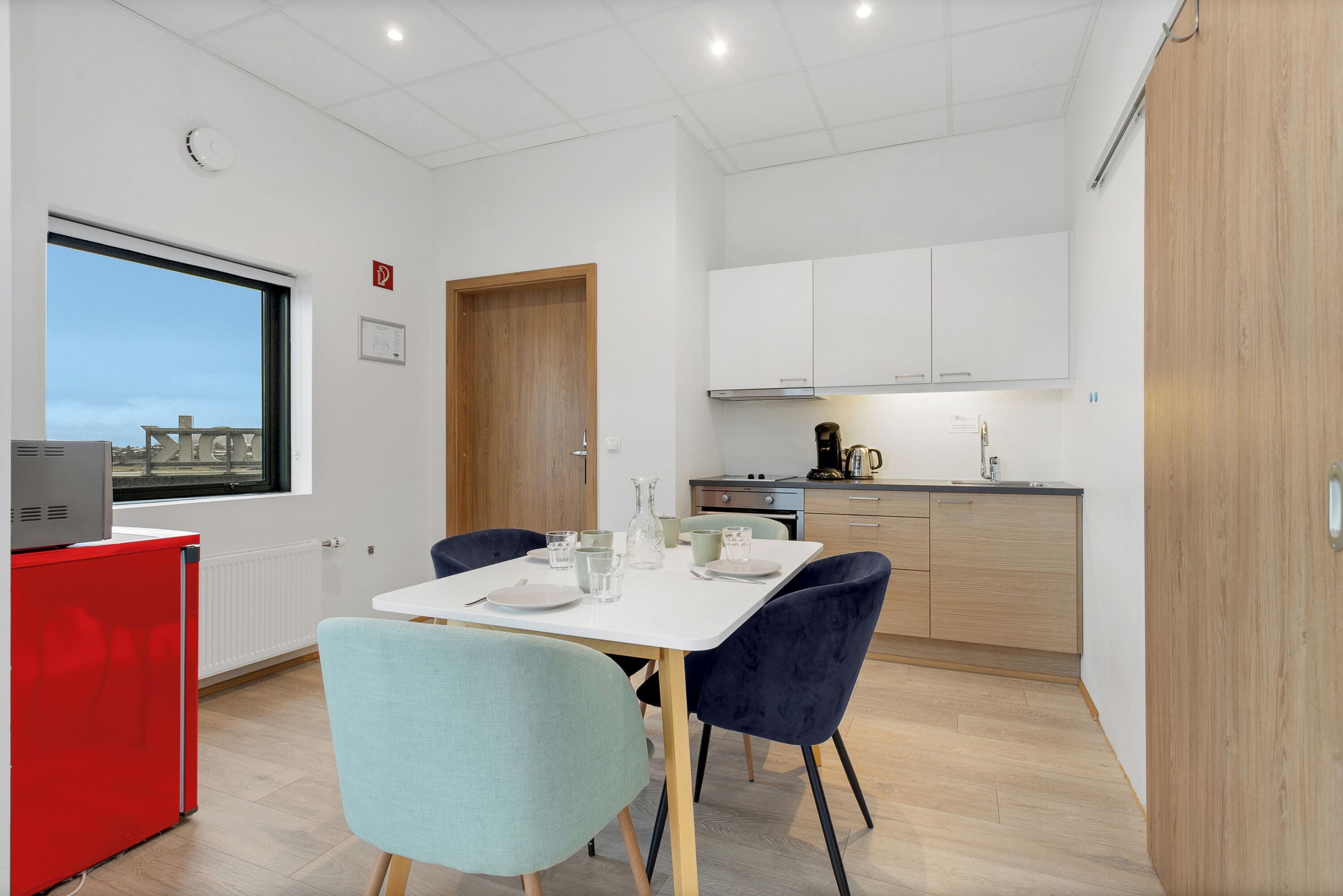A compact kitchen with white cabinets, a red appliance, and a dining area with two chairs and a table set for two.