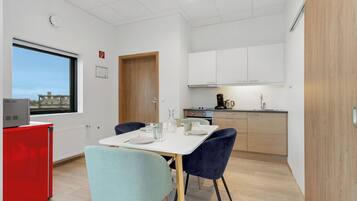 A compact kitchen with white cabinets, a red appliance, and a dining area with two chairs and a table set for two.