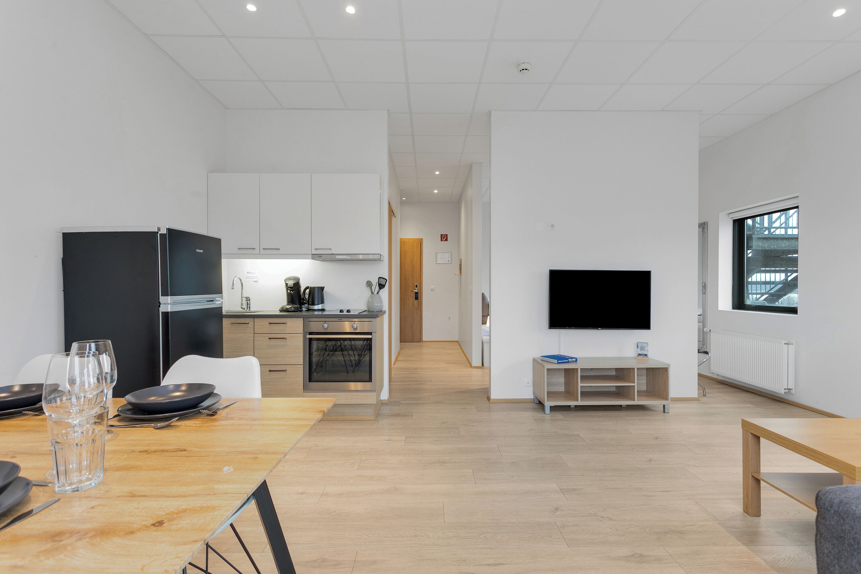 Une cuisine moderne avec un réfrigérateur noir, une table à manger en bois et un téléviseur fixé au mur.