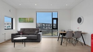 Un salon moderne avec un canapé gris, une petite table blanche et un coin repas comprenant deux chaises et une table.