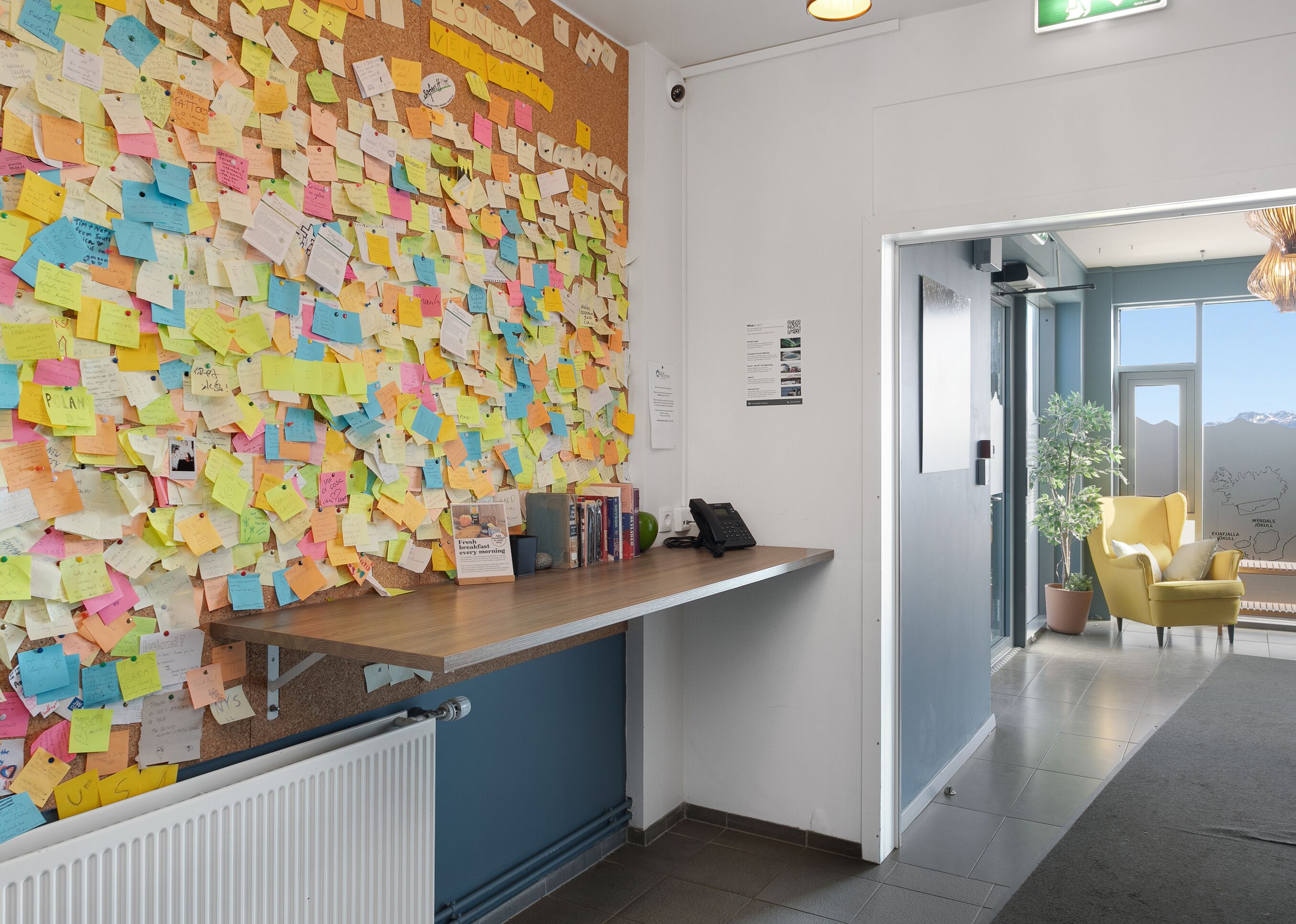 A reception area with a corkboard covered in colorful notes, a reception desk, a phone, and a potted plant.