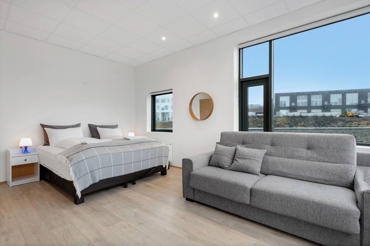 A modern bedroom with a bed, bedside table, and a grey sofa.