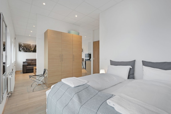 Un dormitorio moderno con una cama grande, un armario de madera y una zona de estar con sofá y sillón.
