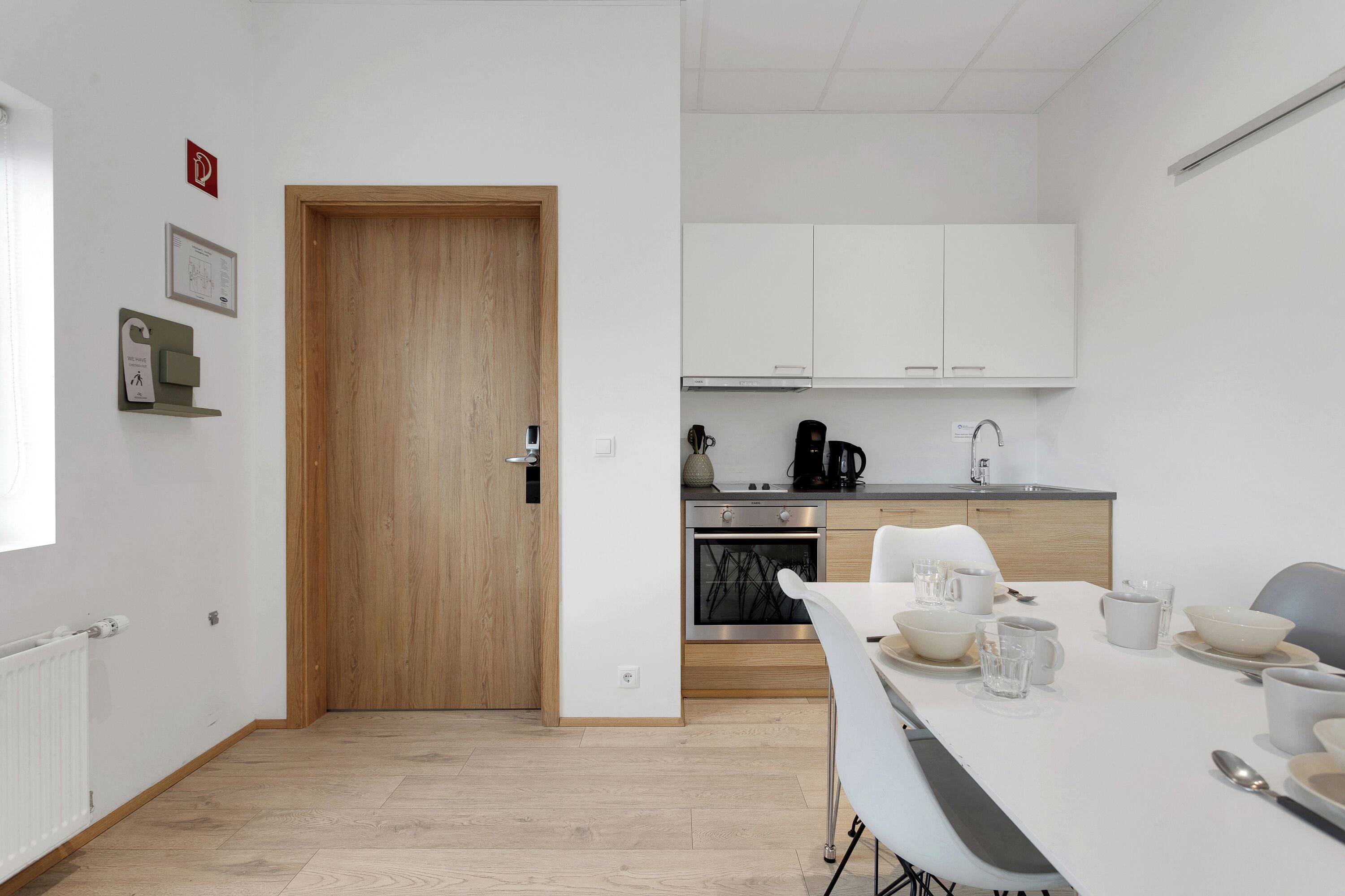 Una cocina moderna con armarios blancos, una puerta de madera y una zona de comedor con una mesa dispuesta para dos comensales.
