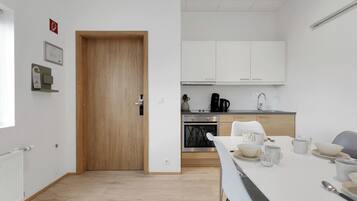 Una cocina moderna con armarios blancos, una puerta de madera y una zona de comedor con una mesa dispuesta para dos comensales.