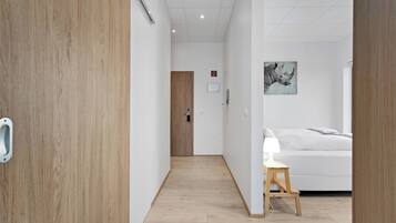 Une chambre d’hôtel avec un plancher en bois, un lit avec une literie blanche, un petit tabouret en bois et une œuvre d’art accrochée au mur.