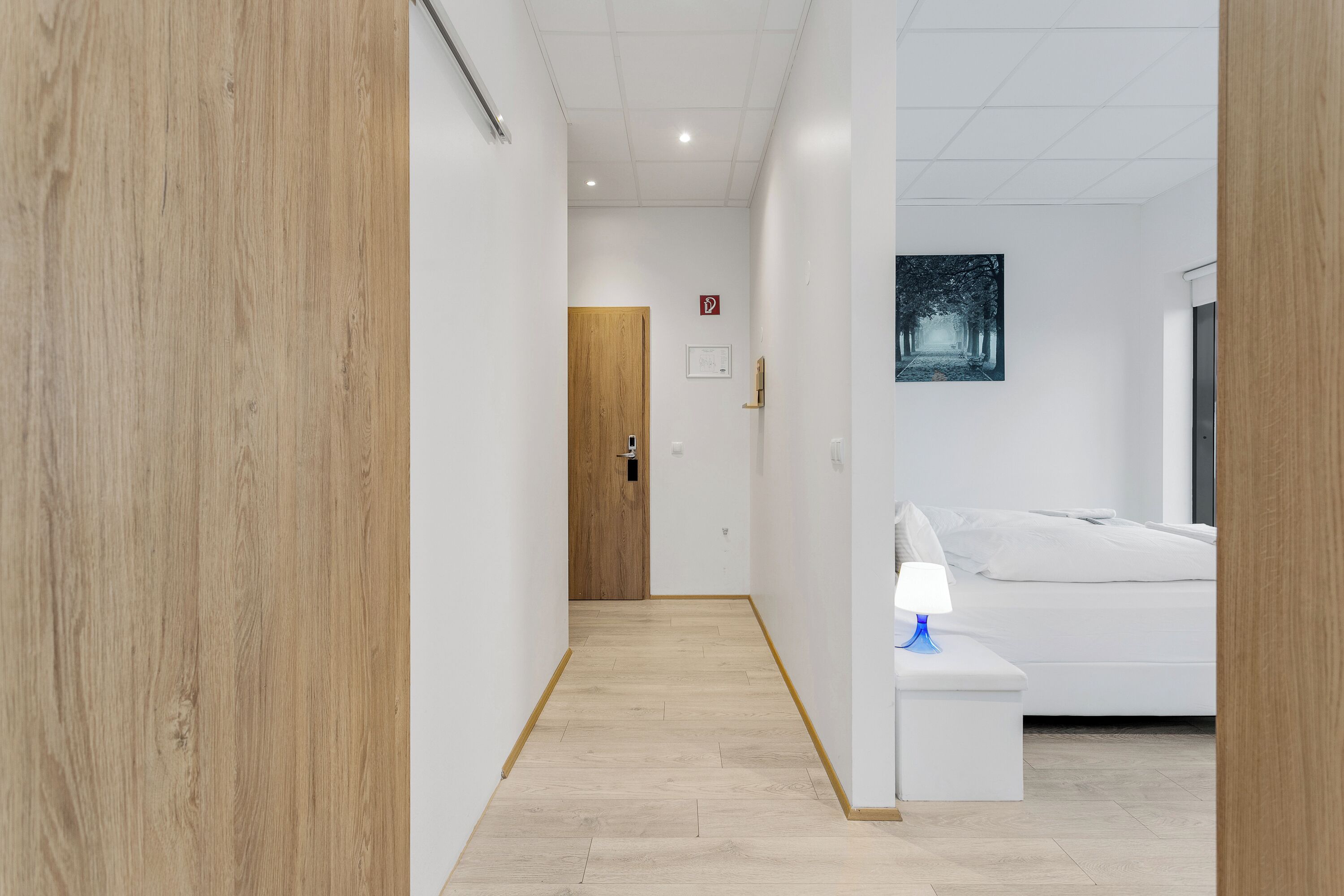 Un pasillo con piso de madera, pared blanca y una puerta al final.