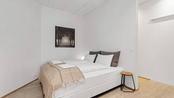 Een minimalistische slaapkamer met een groot bed, een klein krukje en een foto aan de muur.