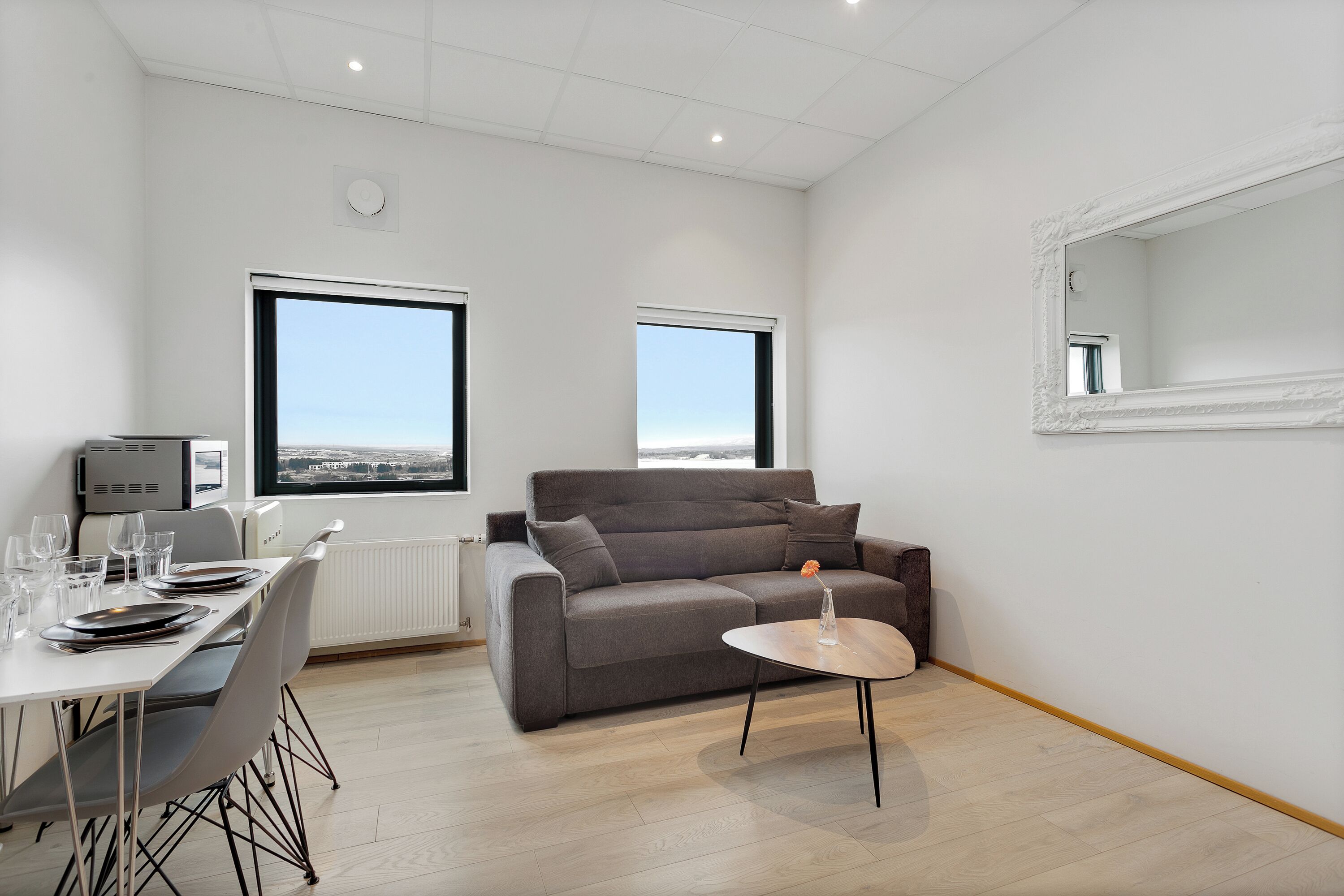 Una sala de estar moderna con un sofá gris, una mesa de comedor con platos y vasos, y una pequeña mesa redonda con una vela.