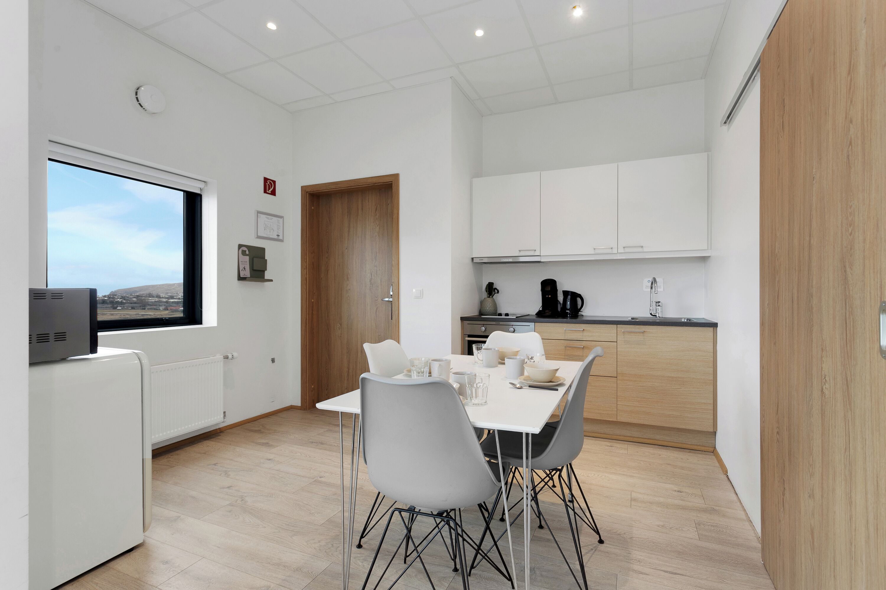 Una cocina moderna con armarios blancos, una mesa de comedor con sillas y vistas a través de una ventana.