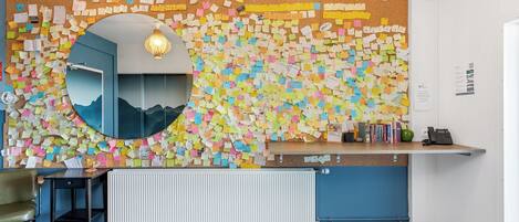 A reception area with a corkboard covered in colorful notes, a round mirror, a desk, and a chair.