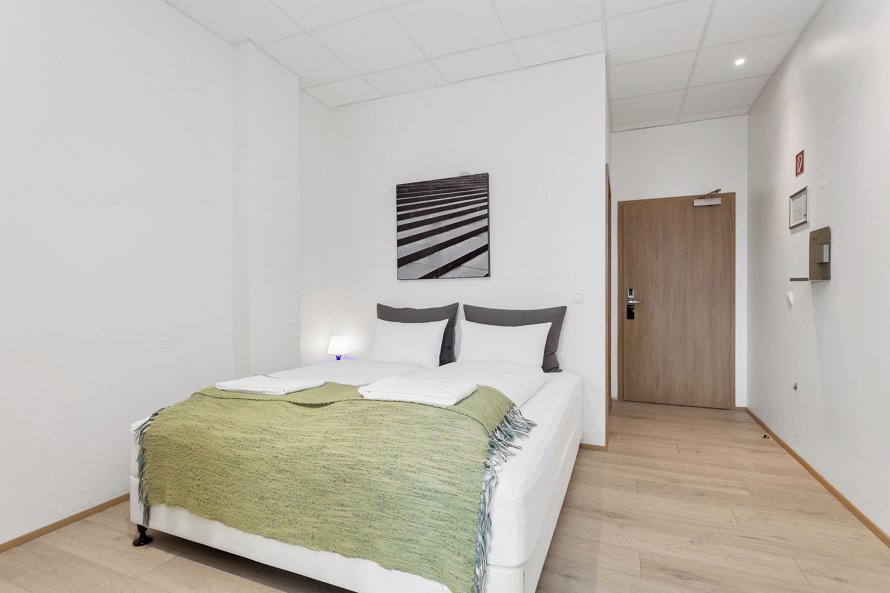 Une chambre à coucher moderne avec un lit, un plaid vert et une œuvre d’art en noir et blanc au-dessus du lit.