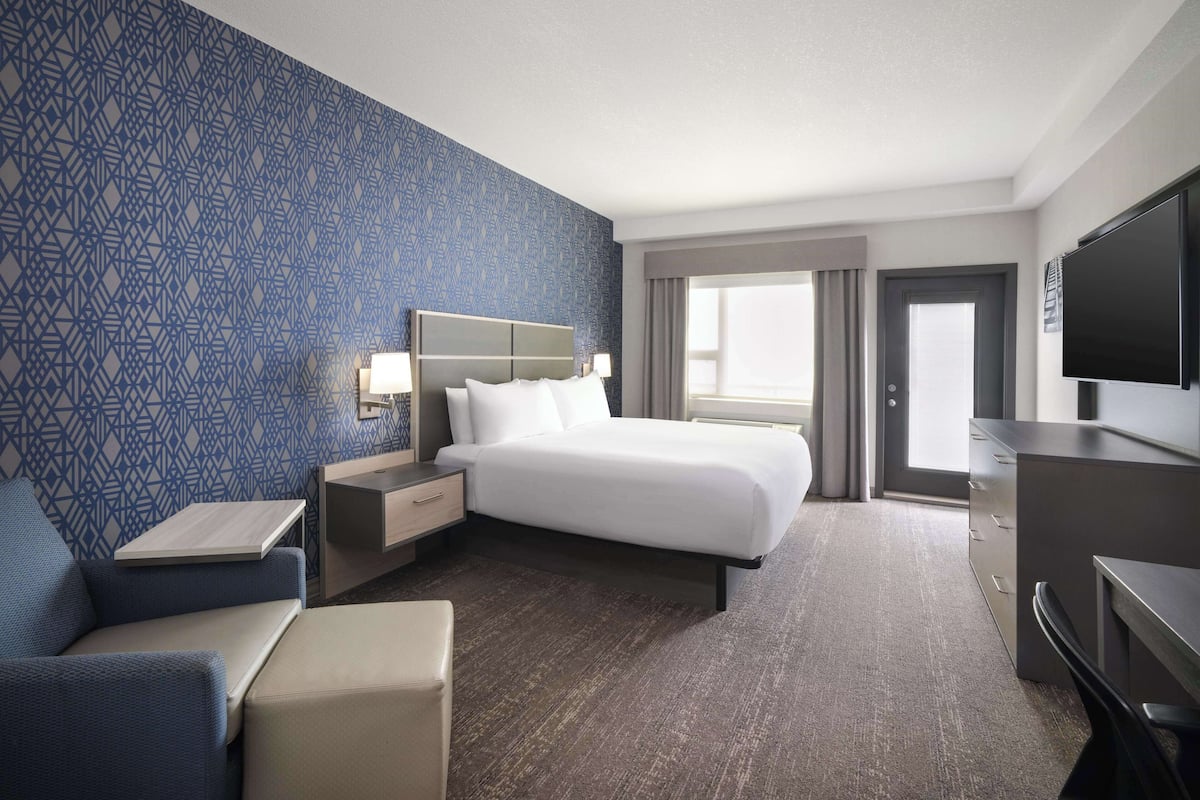 Ein Hotelzimmer mit einem großen Bett, einem Schreibtisch, einem Fernseher und einem Fenster mit Vorhängen.