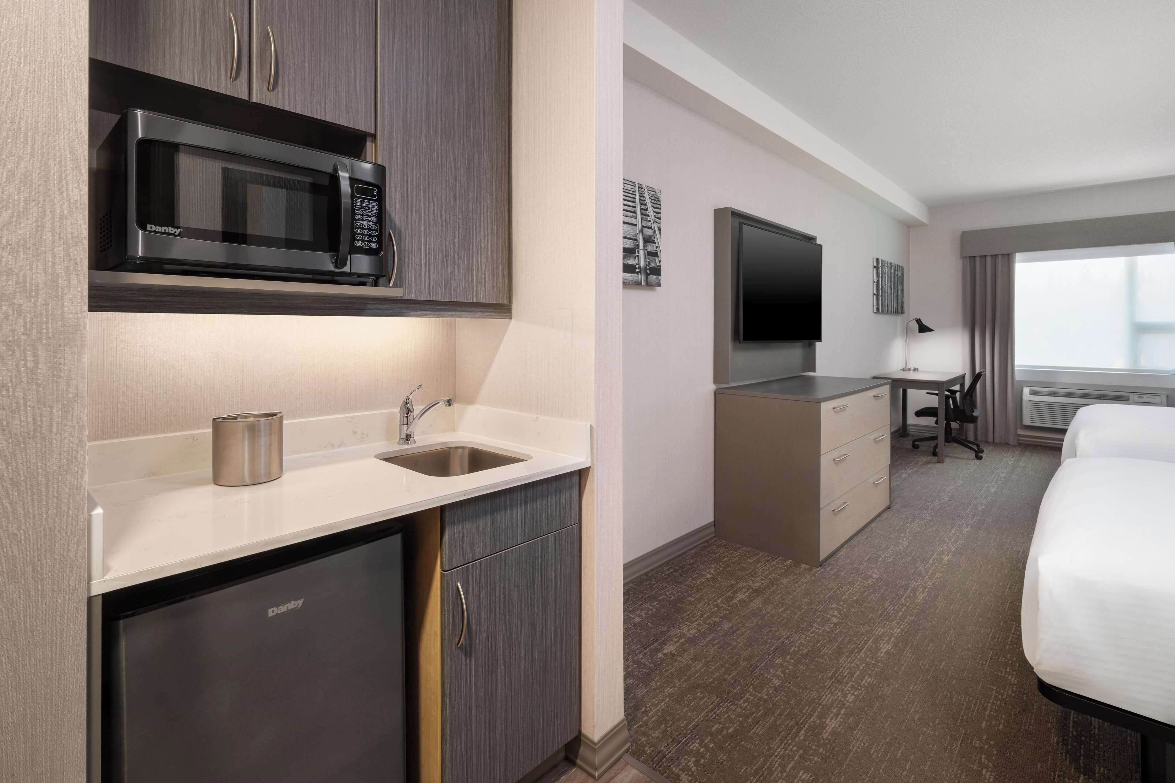 Une chambre d’hôtel moderne dotée d’une petite kitchenette, d’un téléviseur à écran plat, d’un bureau avec une chaise et d’un lit.