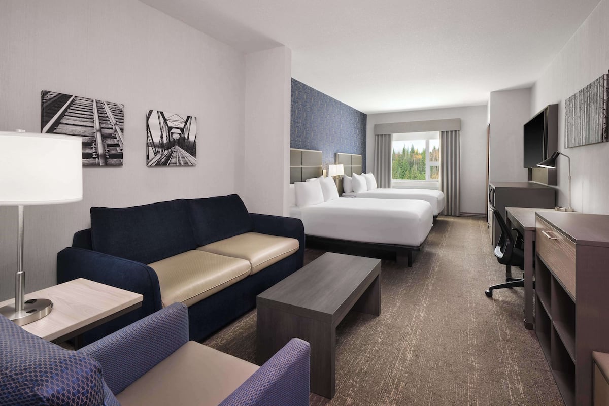 Ein Hotelzimmer mit einer Couch, zwei Betten, einem Schreibtisch, einem Fernseher und Kunstwerken an den Wänden.